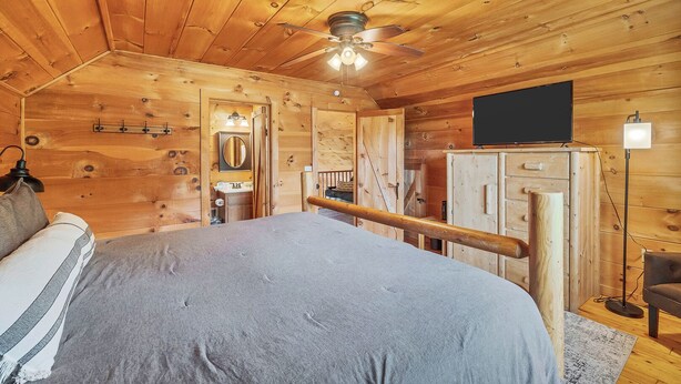 Ein Schlafzimmer einer Holzhütte mit Bett, Deckenventilator, Fernseher und Nachttisch.