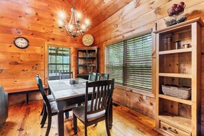 A wooden interior with a dining table, chairs, a chandelier, a clock, and a window with blinds. - Twin Cub Lodge, 3 Br, 2 Ba, Sleeps 8 & Hot Tub (Townsend)