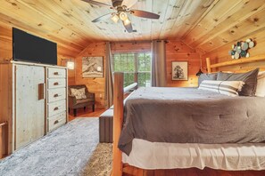 Un dormitorio tipo cabaña de madera con cama, una silla, un escritorio y un ventilador de techo.