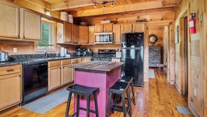 Ein Holzblockhaus-Interieur mit einer Küche, die eine zentrale Kochinsel, Barhocker, eine Mikrowelle, einen Kühlschrank und einen Feuerlöscher umfasst.