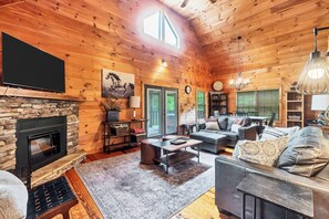 A log cabin interior with a stone fireplace, a television, a sofa, and a dining area. - Twin Cub Lodge, 3 Br, 2 Ba, Sleeps 8 & Hot Tub (Townsend)