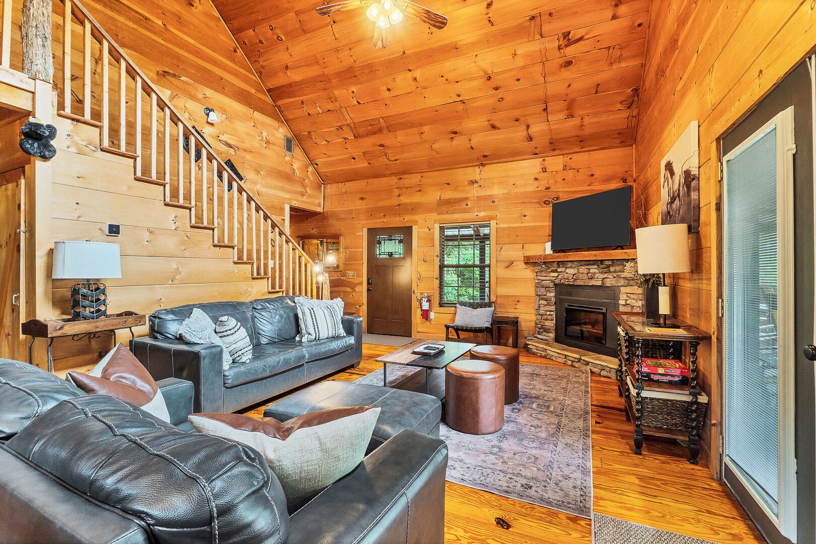 A log cabin interior with a staircase, leather sofas, a fireplace, and a television.