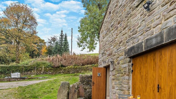 Un bâtiment en pierre avec une porte en bois, un banc en pierre et une table avec des chaises à l’extérieur.