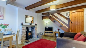 Ein gemütliches Wohnzimmer mit Kamin, Holzbalken, einem Essbereich und einer Treppe.