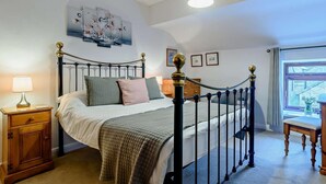 Ein Schlafzimmer mit Himmelbett, Nachttisch, Lampe, Fenster und einem Gemälde an der Wand.