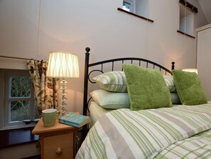 A bedroom with a bed, pillows, a bedside table with a lamp, a book, and a window with curtains. - 1 Bed in Bakewell (oc-pk547) (Ashford in the Water)