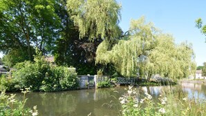 Ein ruhiger Fluss mit Weidenbäumen, einer Steinbrücke und üppigem Grün.