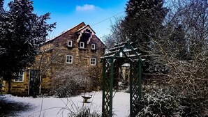 Ein Gebäude aus Stein mit einem geneigten Dach, einer Holzpergola und verschneitem Grund.