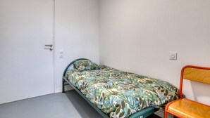 A small, single-bed room with a door, a power outlet, and a chair. - Room with Shared Terrace and Wi-Fi, 10 Minutes from the Beach (Mudaison)