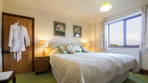 A bedroom with a bed, two bedside lamps, a window with curtains, a wooden door, and a robe hanging on the door. - 2 Bed in Holmesfield (oc-pk783) (Dronfield)