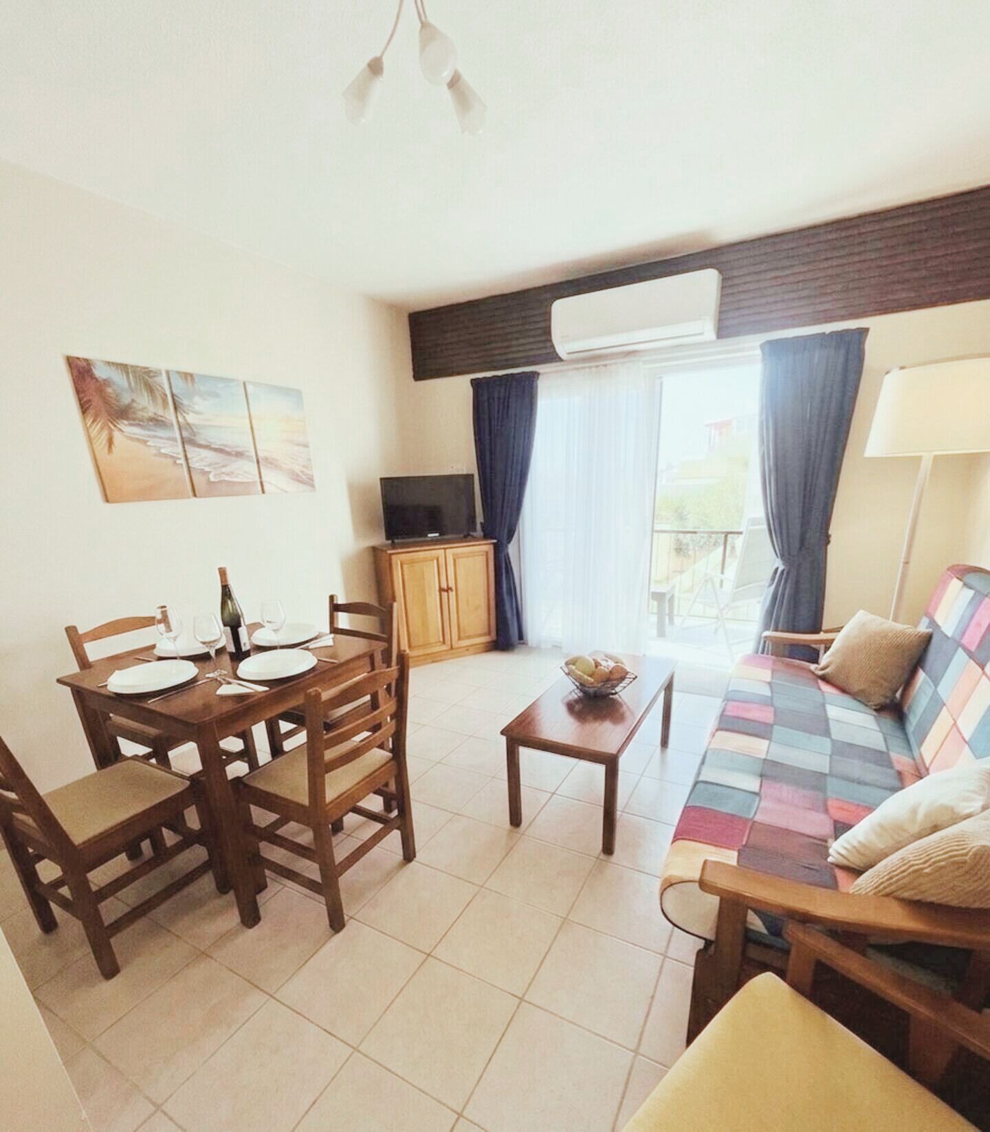 A living room with a sofa, a dining table set for two, a television, and a window with curtains.