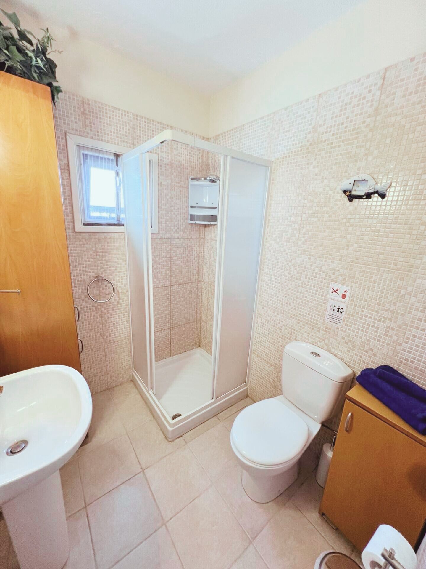 A bathroom with a shower, toilet, sink, and a small window.