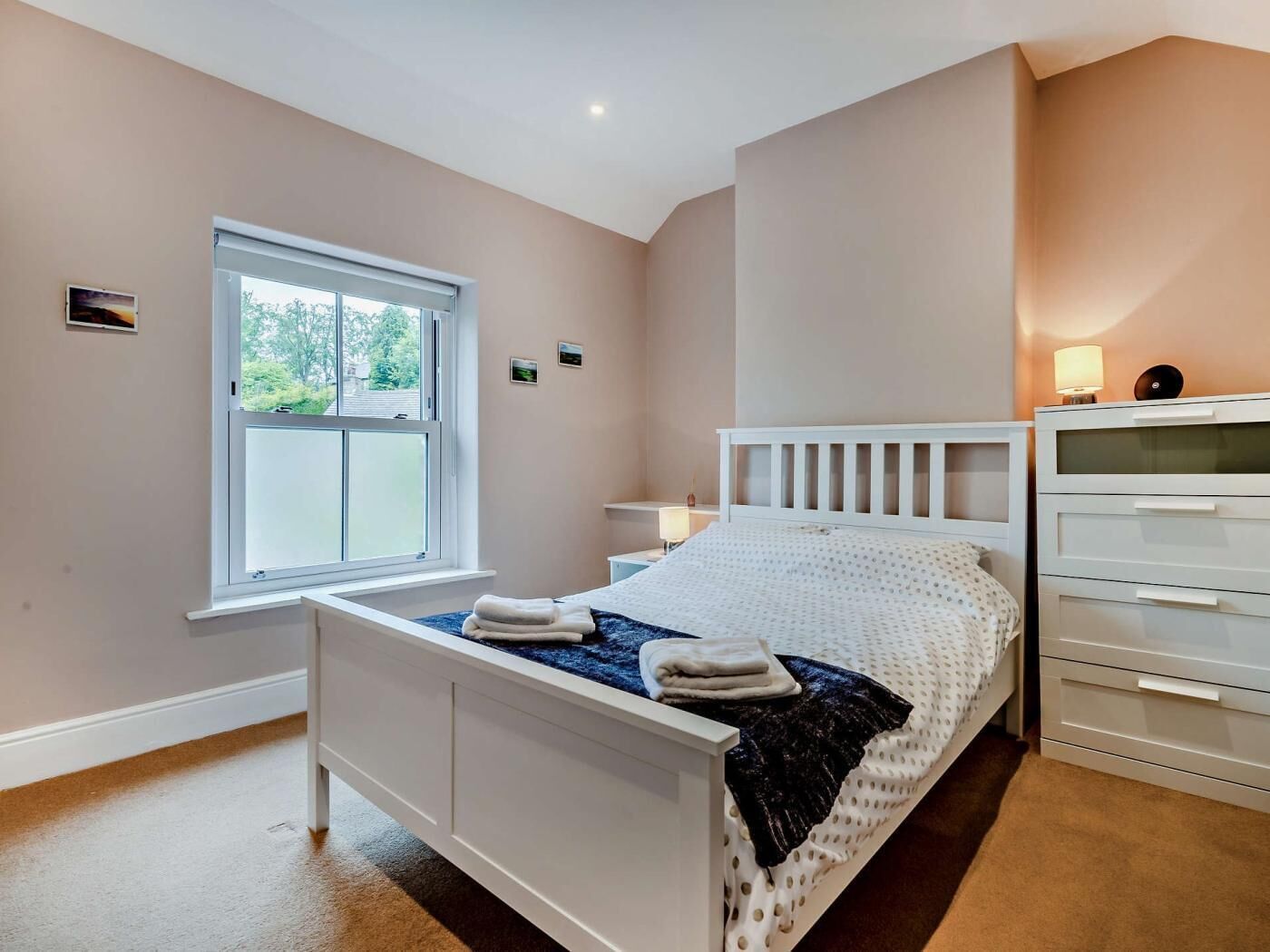 A bedroom with a bed, a window, a bedside table, and a dresser.