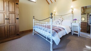 Ein Schlafzimmer mit weißem Metallbettgestell, einem Holzschrank, einem kleinen Nachttisch mit Lampe und einem Spiegel.