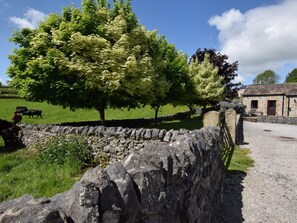 A stone wall, a stone building, and a grassy field with trees and cows. - 1 Bed in Ashford In The Water (oc-pk574) (Ashford in the Water)
