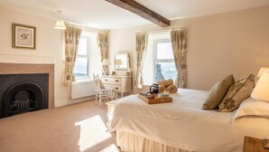 A bedroom with a fireplace, a bed with a tray of fruits, a dresser, and a chair. - 4 Bed in Matlock (oc-pk861) (Holloway)