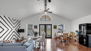 Un salón espacioso con ventilador de techo, una zona de comedor con sillas de madera y una cocina con refrigerador negro.