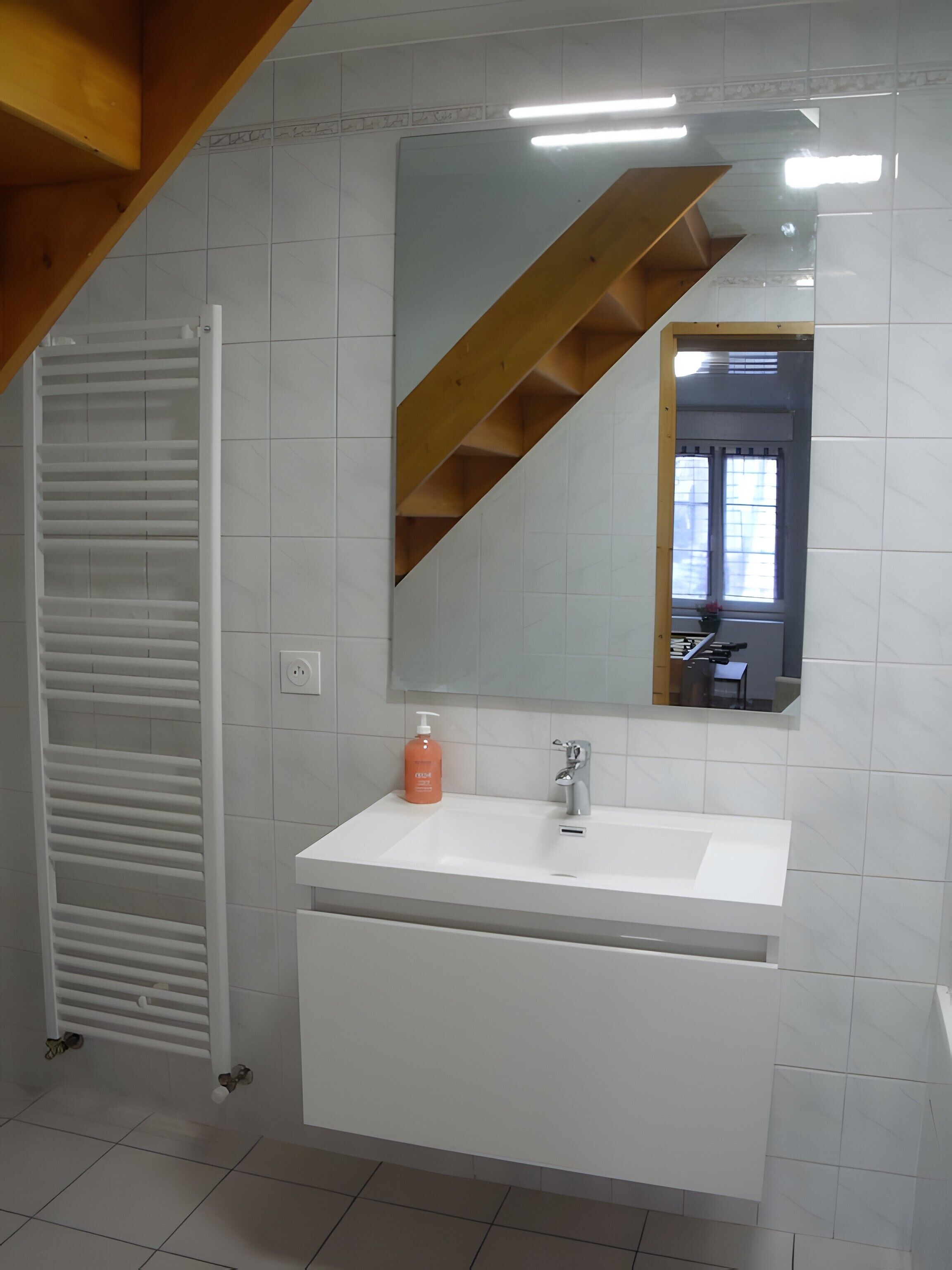 A bathroom with a white sink, a mirror, a wooden staircase, and a radiator.