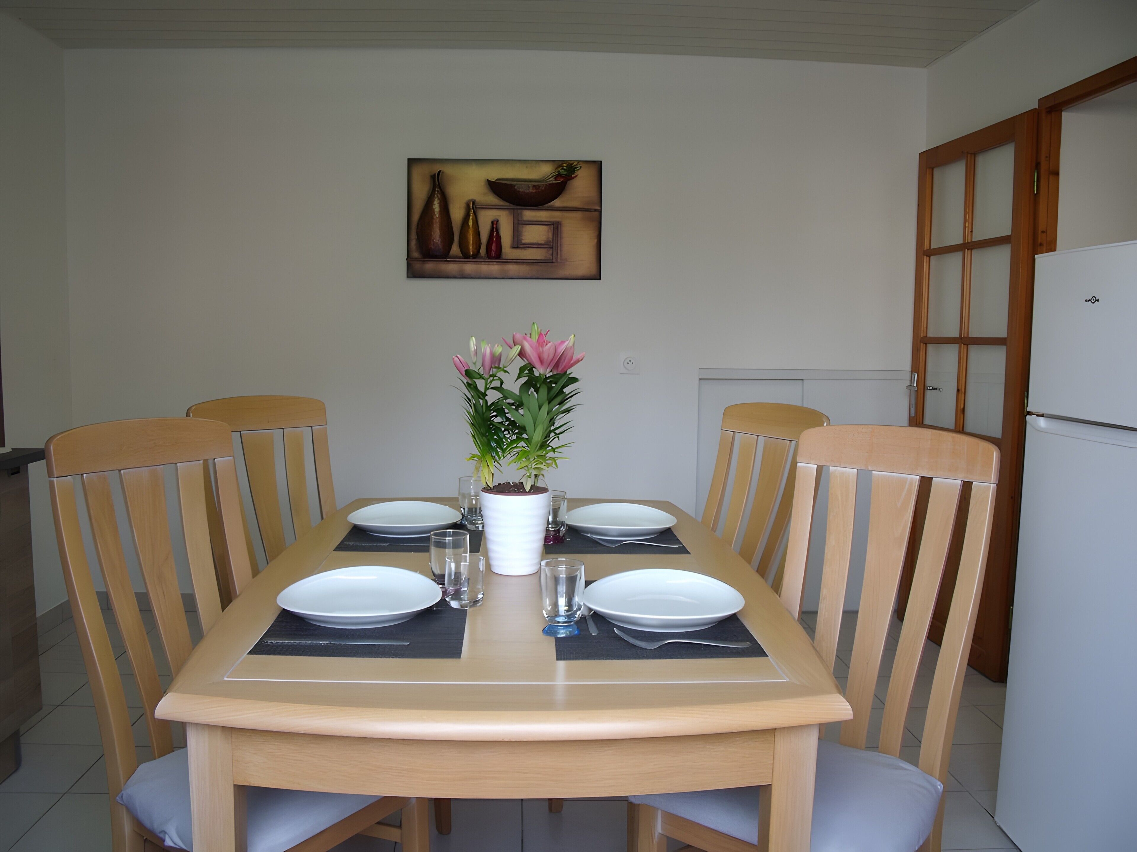 A dining table set for four with chairs, a potted plant, and a painting on the wall.