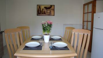 A dining table set for four with chairs, a potted plant, and a painting on the wall.