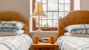 Ein Schlafzimmer mit zwei Betten, einem Nachttisch mit Büchern und einer Lampe sowie einem Fenster mit Blick.