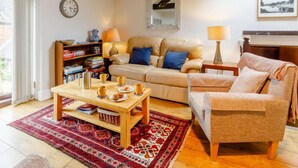 Ein gemütliches Wohnzimmer mit Sofa, Sessel, Couchtisch, Bücherregal und einer Wanduhr.
