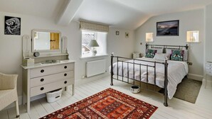 Un dormitorio con cama, cómoda, ventana con vistas, radiador y alfombra.