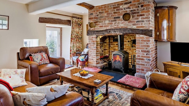 Una sala de estar acogedora con chimenea de ladrillo, sofás de cuero, una mesa de centro de madera y un televisor.