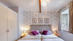 Un dormitorio con dos camas, un armario, pared estampada, cuadros enmarcados y una ventana con cortinas.