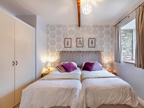 Ein Schlafzimmer mit zwei Betten, einem Kleiderschrank, einer Wand mit Muster, gerahmten Bildern und einem Fenster mit Vorhängen.