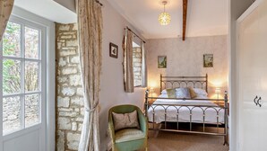 Una camera da letto con un muro in pietra, un letto con struttura in metallo, una sedia verde e una finestra con tende.