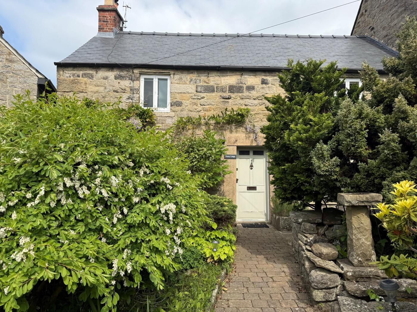 A stone cottage with a white door, a small window, and a brick pathway leading to the entrance.