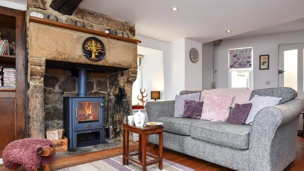 A cozy living room with a stone fireplace, a grey sofa, and a small wooden table. - 3 Bed in Baslow (oc-pk917) (Baslow)