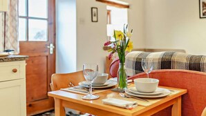 A dining area with a wooden table set for two, a vase with flowers, and a plaid sofa in the background. - 1 Bed in Wirksworth (oc-pk925) (Wirksworth)
