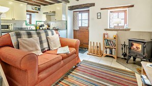 A cozy living room with a sofa, a fireplace, a bookshelf, and a kitchen in the background. - 1 Bed in Wirksworth (oc-pk925) (Wirksworth)
