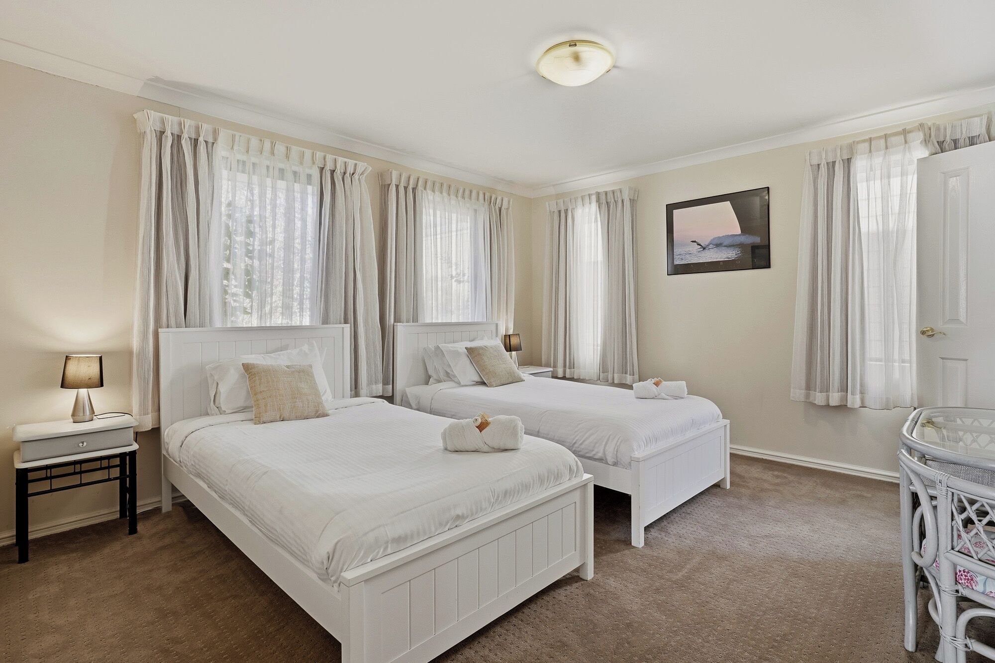 A hotel room with two beds, a small table, a lamp, and a painting on the wall.