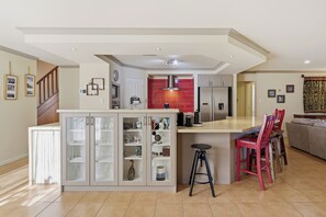A modern kitchen with a central island, a dining area with red chairs, and a staircase leading to another level. - Murray River family retreat with private pool, kayaks, paddleboards and reserve views (South Yunderup)