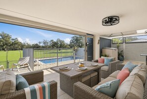 An outdoor patio with wicker furniture, a dining table set, and a view of a swimming pool. - Murray River family retreat with private pool, kayaks, paddleboards and reserve views (South Yunderup)