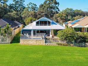 A two-story house with a balcony, surrounded by a well-maintained lawn and a fence. - Murray River family retreat with private pool, kayaks, paddleboards and reserve views (South Yunderup)