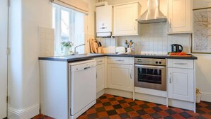 Una cocina compacta con armarios blancos, lavavajillas, horno y suelo a cuadros.