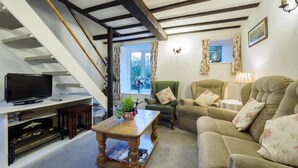 Ein Wohnzimmer mit Fernseher, Couch, Sessel und einem Couchtisch. Eine Treppe mit Fernseher auf der Zwischenebene.