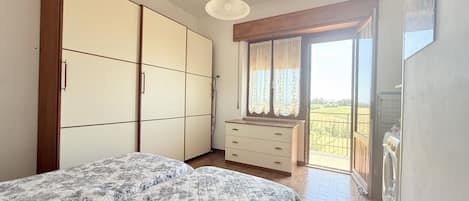 A bedroom with a bed, wardrobe, dresser, and a balcony with a view.