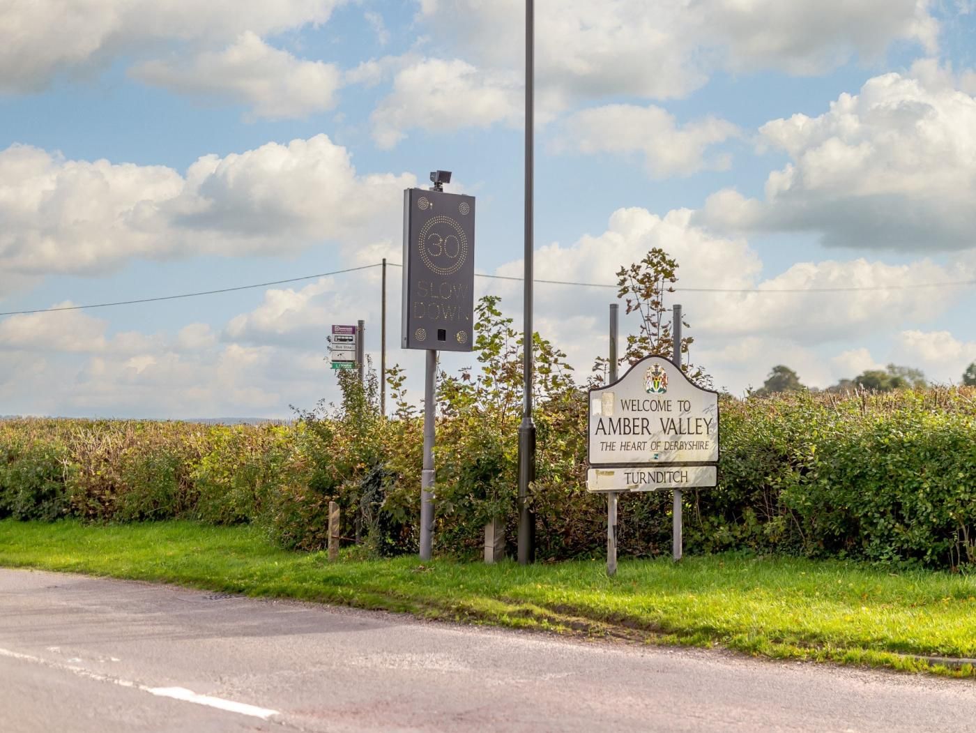 Willkommensschild für Amber Valley, eine Geschwindigkeitsmessanlage und eine Landstraße.