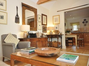 Ein Wohnzimmer mit einer Couch, einem Couchtisch mit Büchern und einer Schüssel, einem Holzschrank und einer Küchenzeile im Hintergrund.