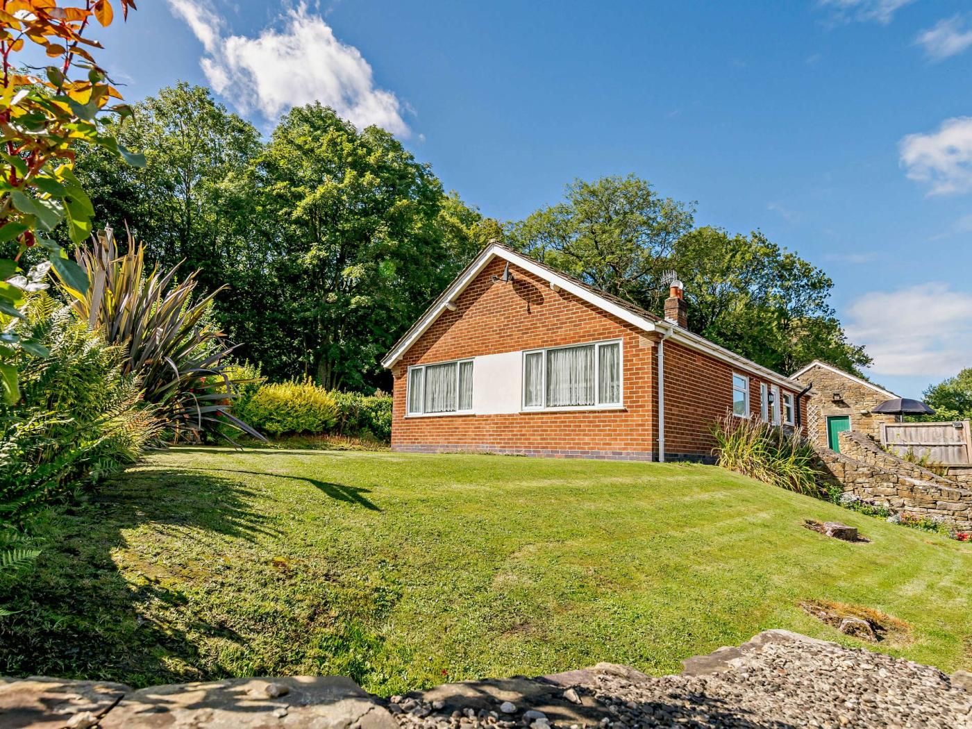 A single-story brick house with a well-maintained lawn and a stone wall.
