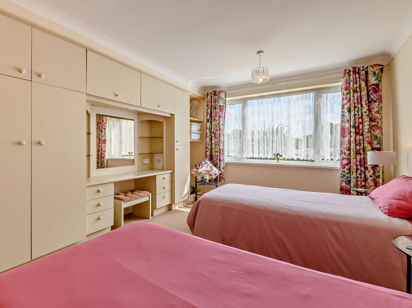 Une chambre avec deux lits, une commode, une coiffeuse avec un miroir et une fenêtre avec des rideaux.