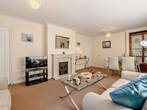 Ein Wohnzimmer mit Fernseher, Kamin, Glastisch und Sitzgelegenheiten.