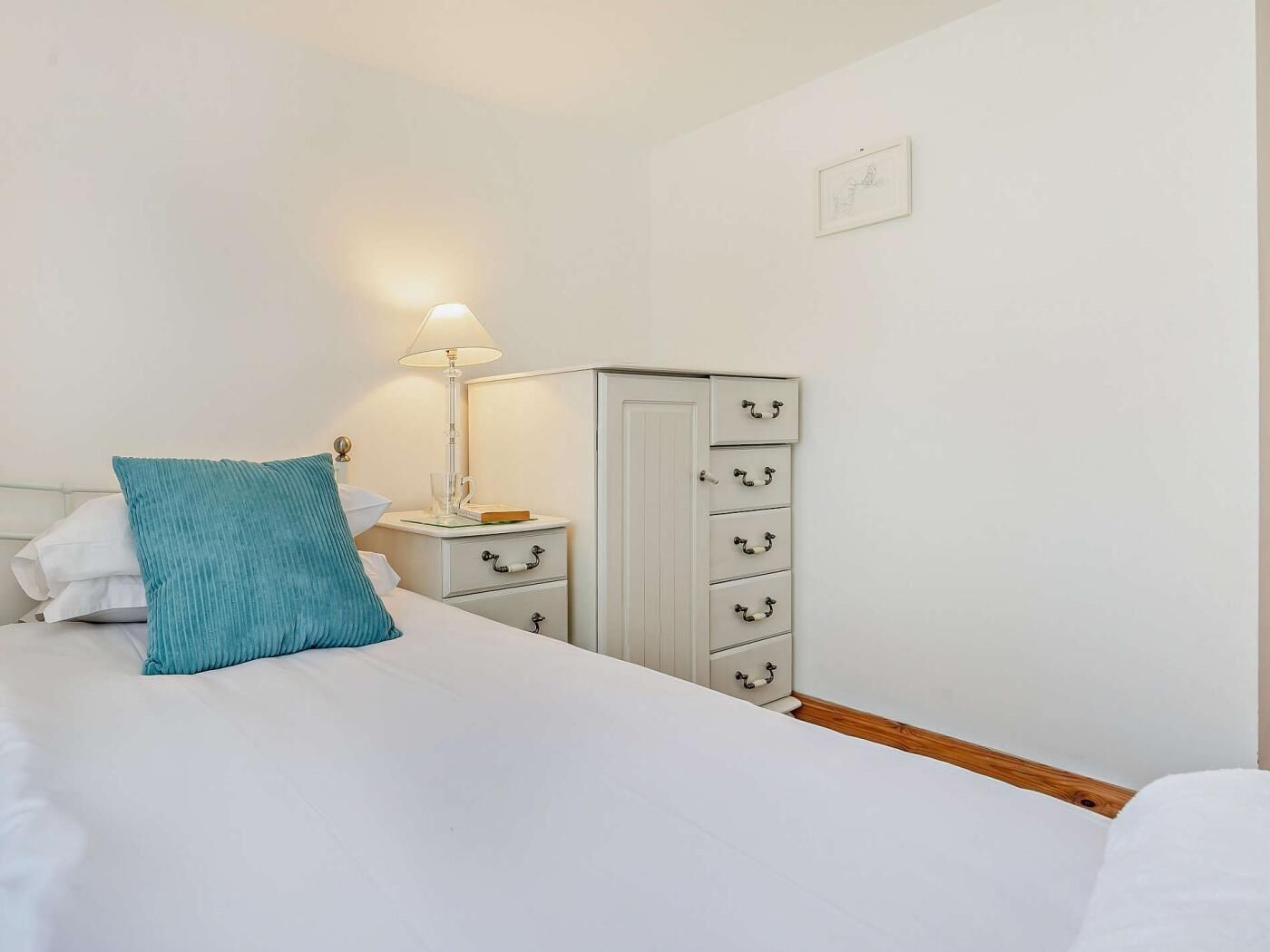 A bedroom with a bed, a bedside table with a lamp, a wardrobe, and a wall-mounted light switch.