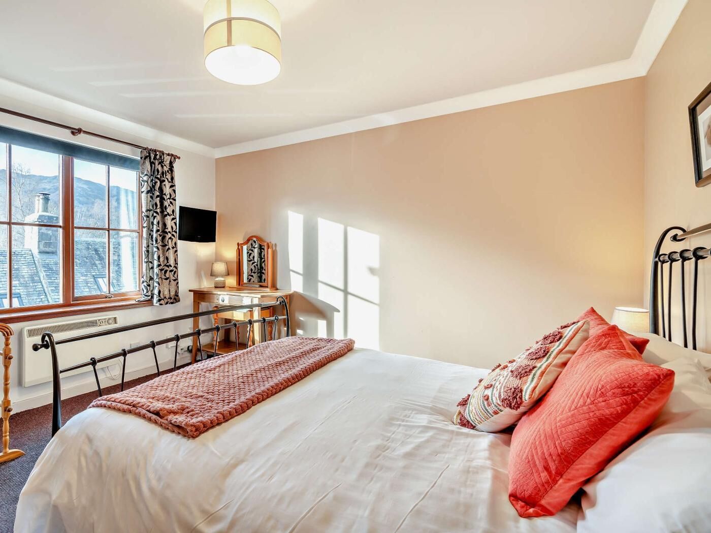 Ein Schlafzimmer mit Bett, Schreibtisch, Stuhl, Heizkörper und einem Fenster mit Vorhängen.