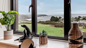 A window with a view of a coastal landscape, a potted plant, a decorative vase, and a black object on the windowsill. - 2 Bed in Helston (oc-45739) (Kuggar)